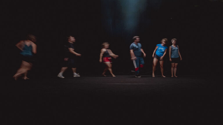 Salle 3 du Labo Victor Hugo. Groupe de personnes en mouvement sur une scène sombre lors d’une répétition artistique au Labo Victor Hugo. Le flou de mouvement traduit la dynamique du travail chorégraphique.