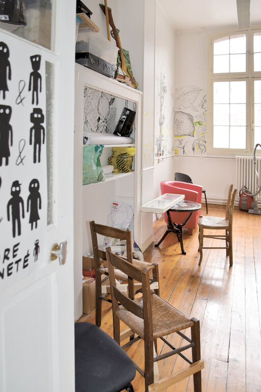 Petit espace de travail du Labo Victor Hugo avec plancher en bois, étagères intégrées, mobilier hétéroclite et dessins muraux réalisés par des artistes en résidence.