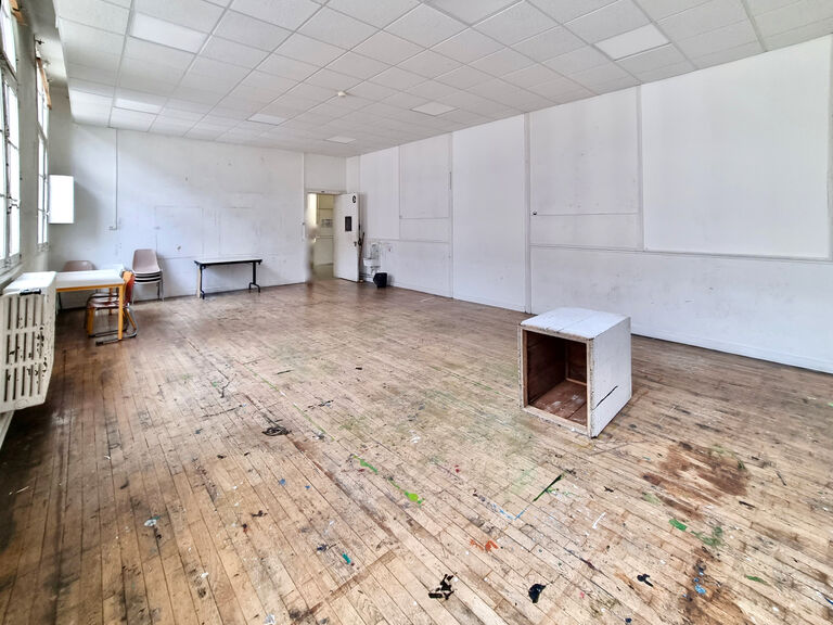 Atelier du Labo Victor Hugo au parquet en bois marqué par l’usage, vaste espace vide destiné aux activités artistiques, avec quelques tables et chaises en périphérie.